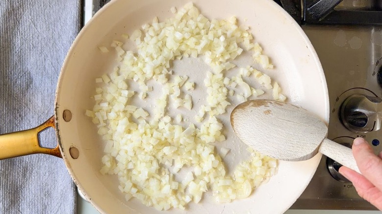 Sautéing chopped yellow onion and garlic in butter in skillet on stovetop