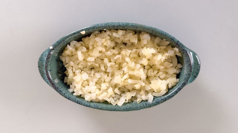 Chopped and cooked yellow onion and garlic cooling in shallow dish
