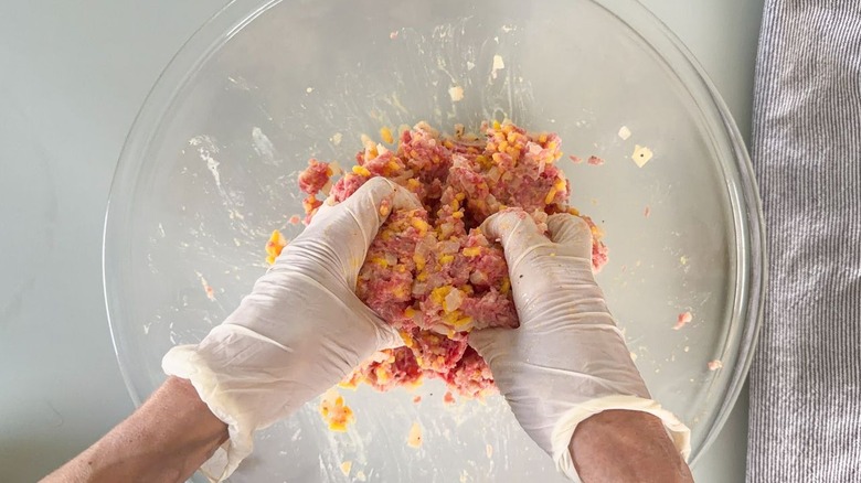 Mixing Swedish-inspired stuffed cabbage roll filling with gloved hands in glass bowl