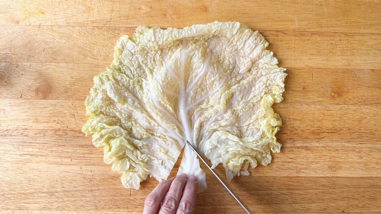 Cutting the stem end from a large blanched savoy cabbage leaf on a cutting board