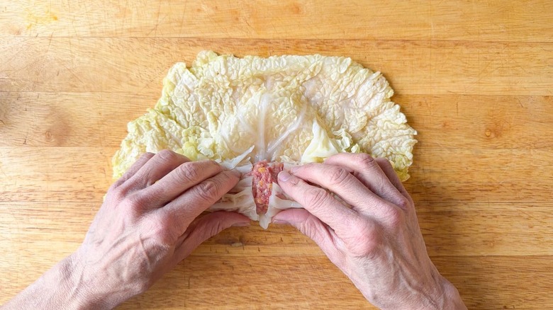 Folding blanched cabbage leaf base over meat filling on cutting board
