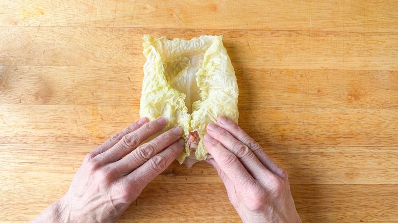 Folding in sides of cabbage leaf while making stuffed cabbage roll on cutting board