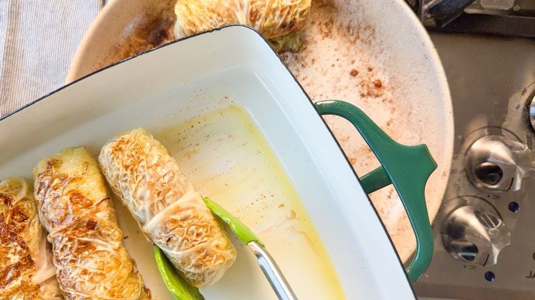 Placing browned Swedish-inspired stuffed cabbage rolls in oiled baking dish with tongs
