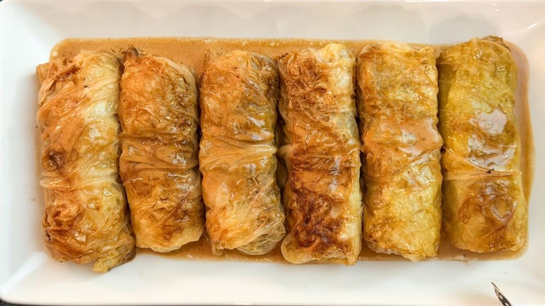 Swedish-inspired stuffed cabbage rolls on white platter with pan sauce