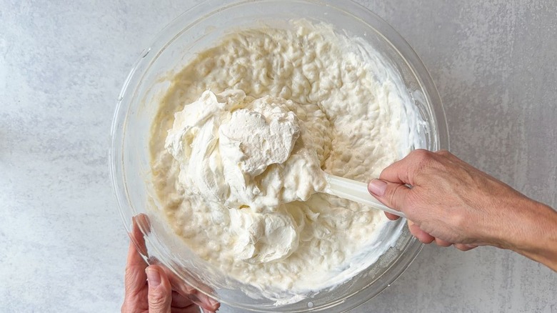 Folding whipped cream into Swedish-style rice pudding in large glass bowl using rubber spatula