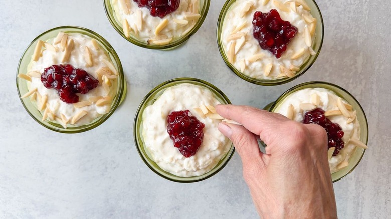 Sprinkling slice almonds onto Swedish style rice pudding in glasses with lingonberries