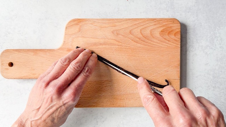 Splitting vanilla bean on cutting board with paring knife tip