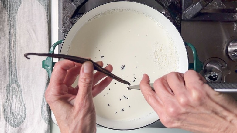 Scraping vanilla bean seeds into large saucepan filled with milk on stovetop