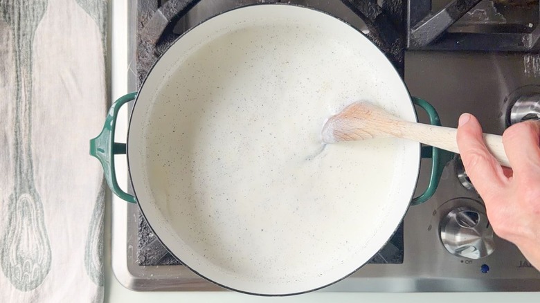 Stirring milk with vanilla bean seeds coming to a boil in large saucepan on stovetop