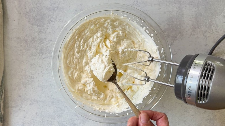 Cream whipped to soft peaks by hand mixer in glass bowl