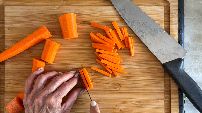 hand slicing carrots on cutting board