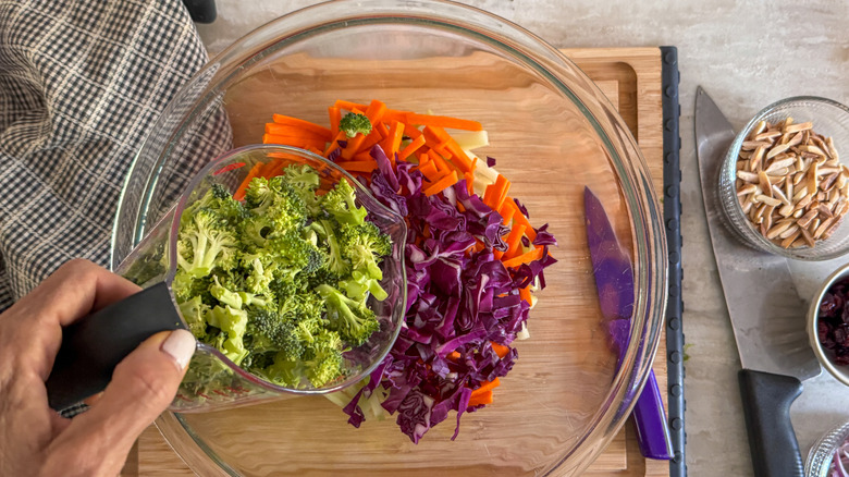 hand adding broccoli to bowl with other slaw ingredients
