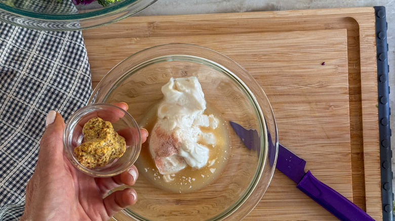 hand adding mustard to bowl with mayonnaise