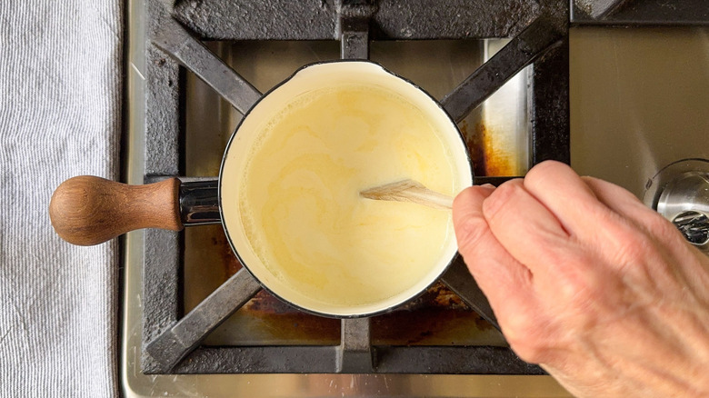 Stirring hot butter and cream in saucepan with wooden spoon