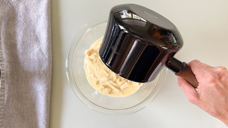 Pouring hot cream over chopped white chocolate in glass bowl