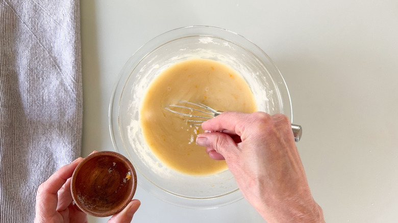 Adding lemon zest and salt to white chocolate ganache in glass bowl