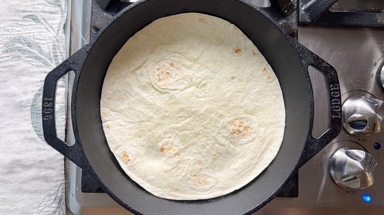 Flour tortilla heating in cast iron skillet on stovetop