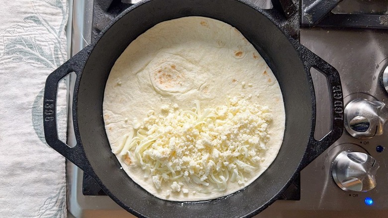 Flour tortilla and shredded cheese in cast iron skillet on stovetop