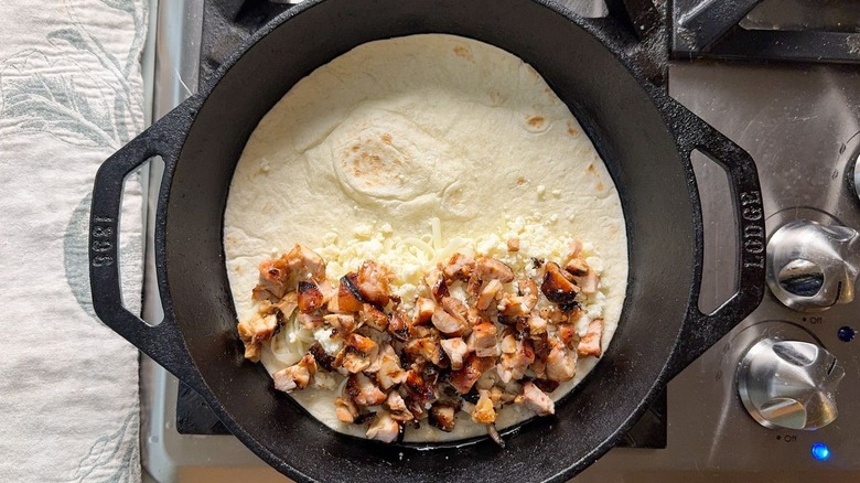 Flour tortilla with chopped chicken and cheese in cast iron skillet