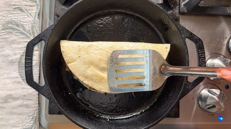 Folded quesadilla in cast iron skillet with metal spatula