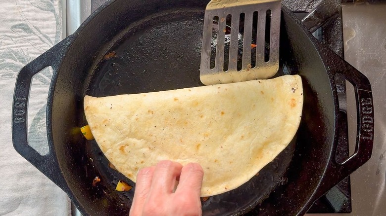 Flipping a quesadilla with a metal spatula in a cast iron skillet