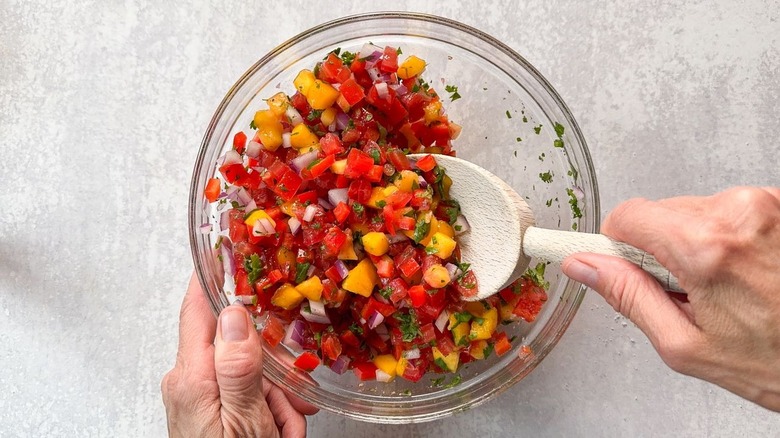 Mixing fresh peach pico de gallo in glass bowl with wooden spoon
