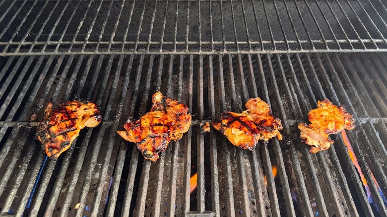 Chicken thighs with grill marks cooking on grill grates