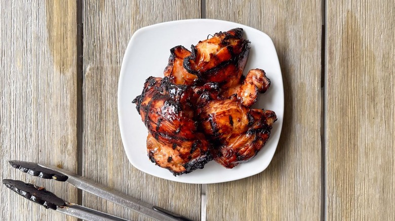 Grilled chicken thighs on plate with tongs