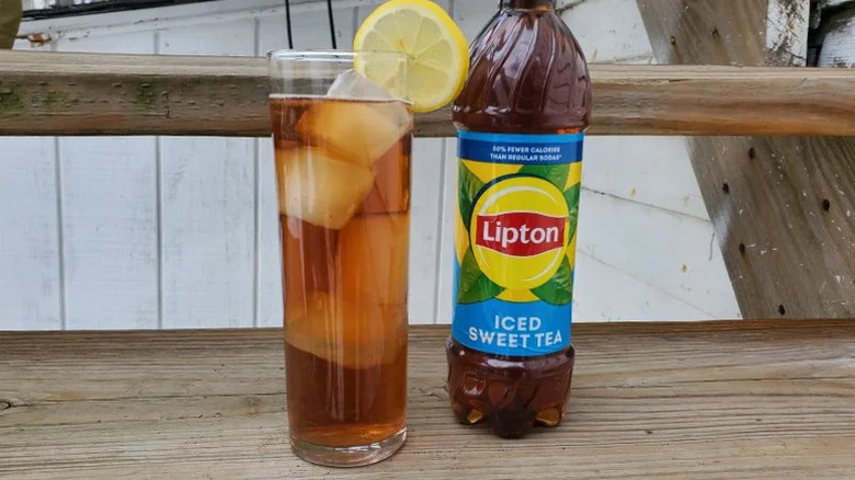 A bottle of Lipton Sweet Tea stands next to a glass of the same iced tea with a lemon.