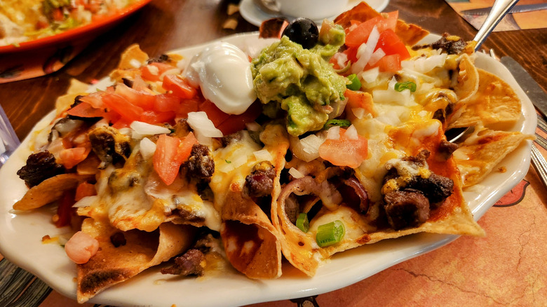 A large plate of nachos with many ingredients.