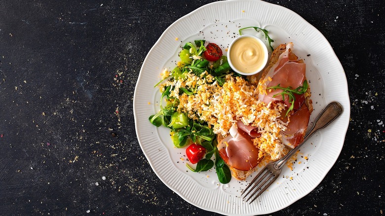 Toast with prosciutto, grated egg, and greens on white plate