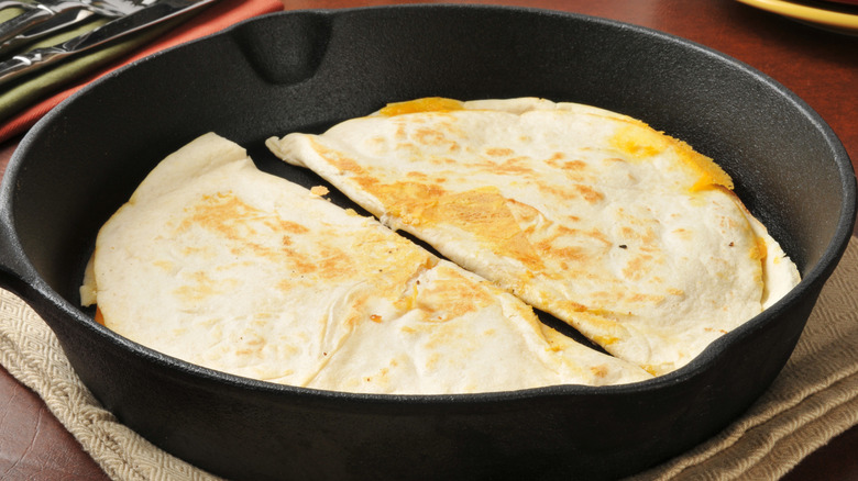 A skillet with two folded quesadillas that's still lightly browned.