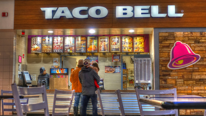 View of counter at a Taco Bell in a mall, with people at the registers ordering