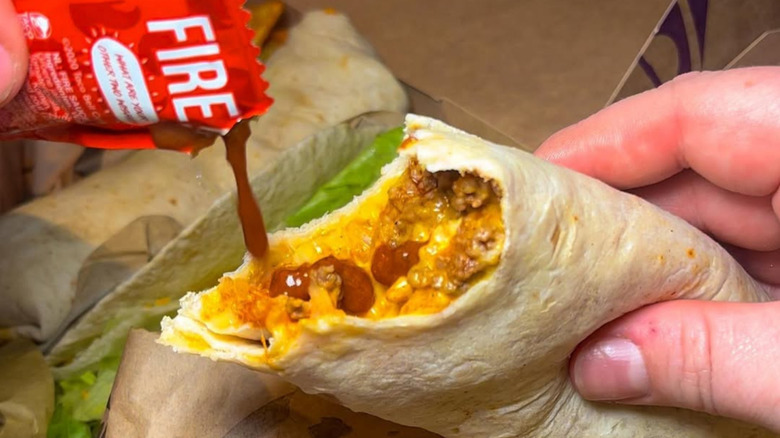 Person adding hot sauce to a Taco Bell burrito