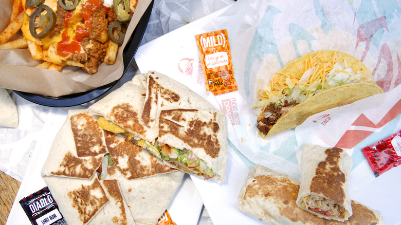 A Taco Bell meal with a crunchy taco, two crunch wraps, two burritos, and fries along with different hot sauce packets