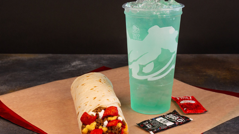A Mountain Dew Baja Blast from Taco Bell next to a burrito and hot sauce packets