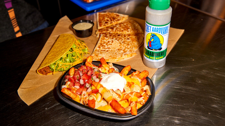 Taco Bell's Secret Aardvark Nacho Fries next to a taco, hot sauce bottle, and quesadilla