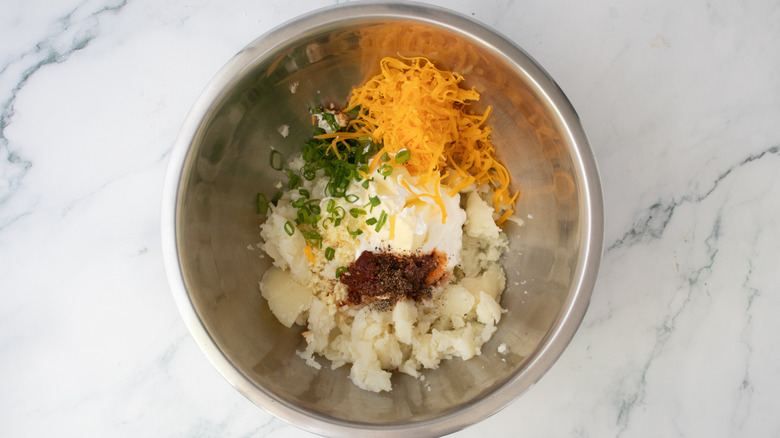 A large bowl filled with cooked potato, cheese, and an assortment of seasonings