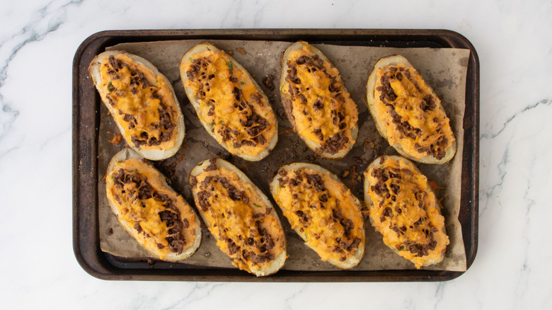 Twice baked potatoes on a large baking sheet topped with cheese and taco beef