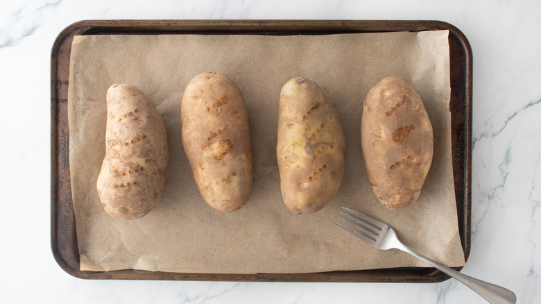 Four large baking potatoes pricked with a fork on baking sheet