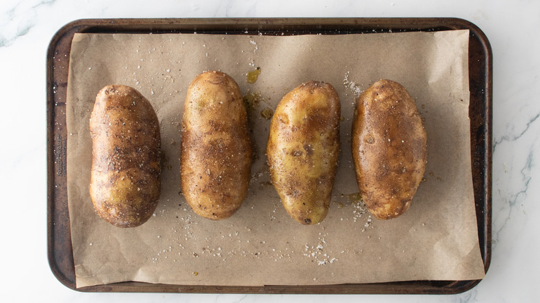 Four large baking potatoes, oiled and seasoned, on a large baking sheet.