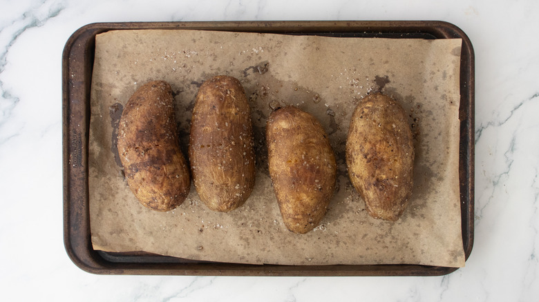 Four well-seasoned baked potatoes on a large baking sheet