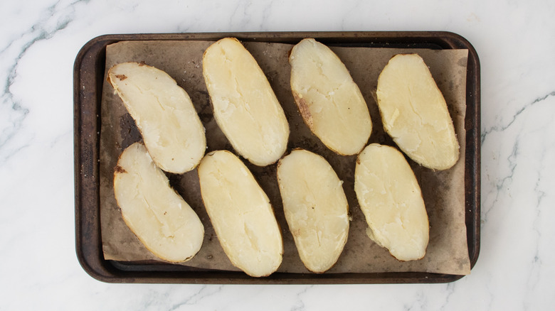 Four halved baked potatoes on a large baking sheet