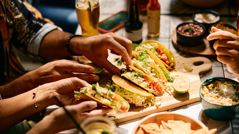 Hands are seen reaching for tacos on a platter.