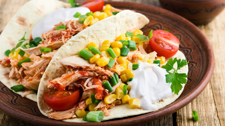 shredded chicken tacos topped with corn, tomatoes, and sour cream
