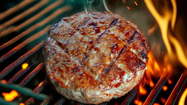 Juicy hamburger patty on a gill surrounded by flame