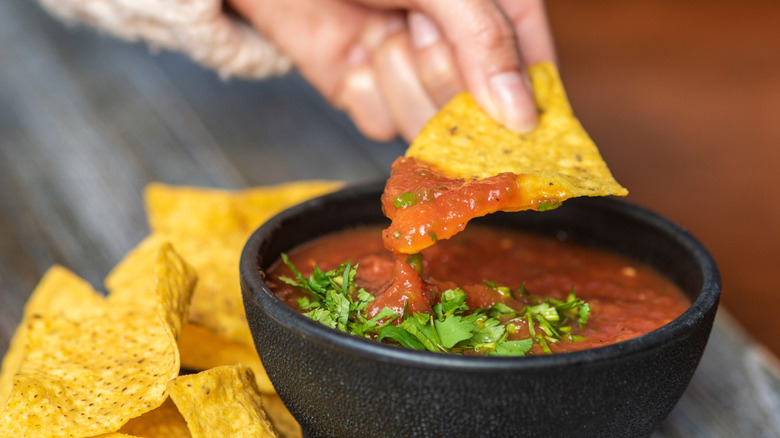 Hand dipping a tortilla chip into a black bowl of salsa