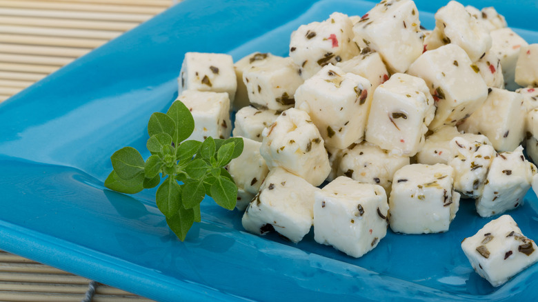 Marinated fresh mozzarella covered in herbs on a blue plate, with a sprig of fresh basil.