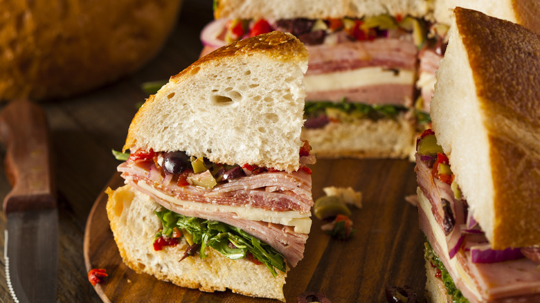 A traditional Muffuletta sandwich cut into quarters on a wooden board.