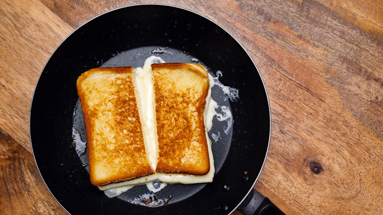 A buttery grilled cheese sandwich sliced in half in a nonstick skillet.